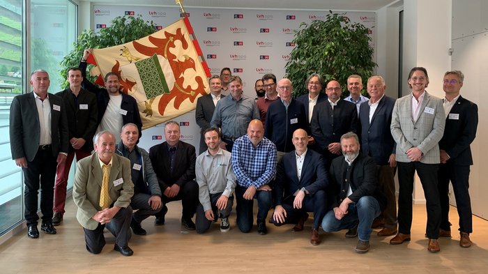 VEUKO-Kongress der Hafner/innen: Für die Zukunft des Kachelofens in Europa Gruppenfoto von Männern in Businesskleidung mit Fahne und Pflanzen im Hintergrund