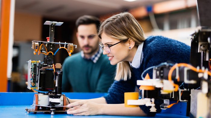 Neue Beiträge für Unternehmen, die weibliche Lehrlinge in MINT-Berufen beschäftigen Frau und Mann prüfen Roboter in einer Technikwerkstatt