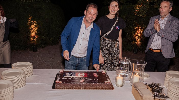 Generation-H Aperitif Mann schneidet Kuchen bei Abendfeier mit zwei weiteren Personen
