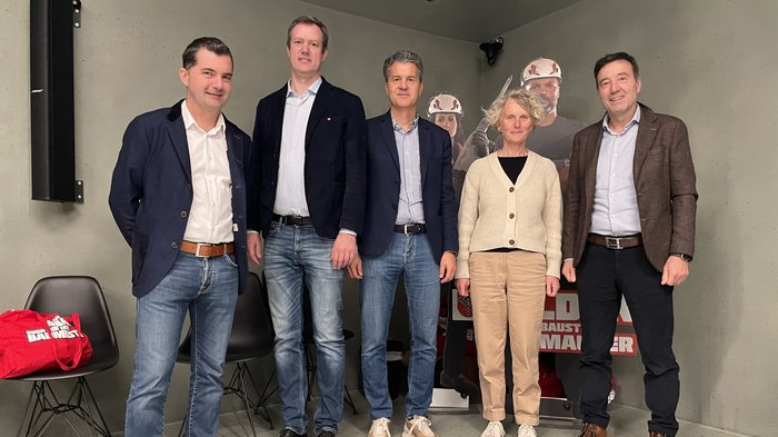 „Multitalent Beton“: Fachveranstaltung setzt starkes Zeichen für nachhaltiges Bauen Fünf Personen stehen in einem Raum vor einer Baustellenwerbung