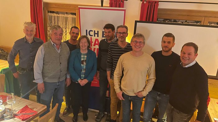 lvh-Ortgruppe Kaltern wählt neuen Obmann Gruppenfoto von neun Personen in einem Raum vor einem Poster und Fenstern mit roten Vorhängen