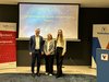 Home Tre persone davanti a schermo con presentazione su investimenti e striscioni bancari
