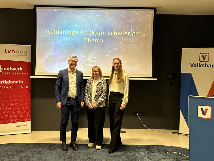 Geldanlage ist (k)ein Thema – Frauen im Handwerk setzen auf finanzielle Kompetenz Drei Personen stehen vor einer Leinwand mit Vortrag zu Geldanlage und Bankenbanner