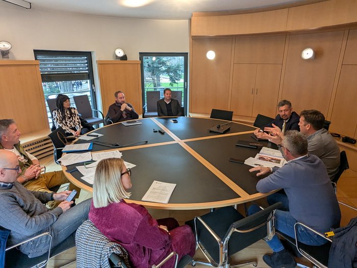 Tiefbau-Unternehmen befürworten digitale Straßenlisten für mehr Planbarkeit Neun Personen sitzen an einem runden Tisch in einem Besprechungsraum.