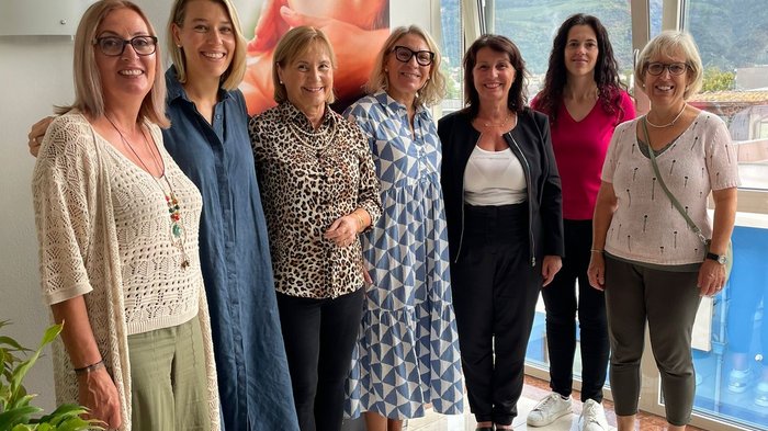 Frauen entdecken Traditionsbetriebe Sieben lächelnde Frauen stehen nebeneinander in einem hellen Raum vor einem Fenster.