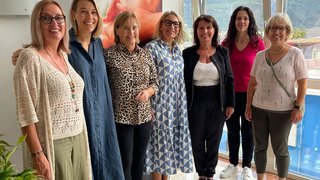 News Sieben lächelnde Frauen stehen nebeneinander in einem hellen Raum vor einem Fenster.