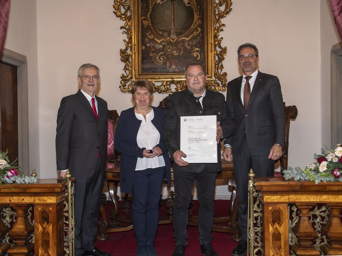 Südtiroler Wirtschaftspreis: Viel Ehre für das Handwerk Vier Personen posieren mit einer Urkunde in einem festlichen Raum mit Blumen