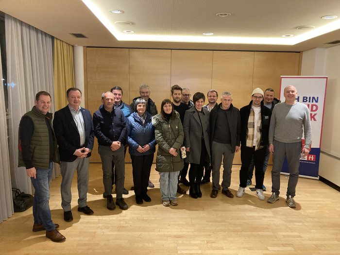 Beständigkeit im Handwerk in Vintl Gruppenfoto von 15 Personen in einem Raum mit Holzfußboden und Vorhängen