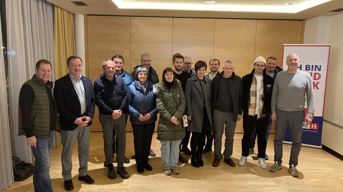 Beständigkeit im Handwerk in Vintl Gruppenfoto von 15 Personen in einem Raum mit Holzfußboden und Vorhängen