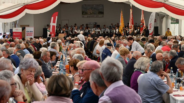 61° incontro degli artigiani anziani a Lutago: un'esperienza indimenticabile Molte persone sedute a un grande evento con musica dal vivo in una tenda