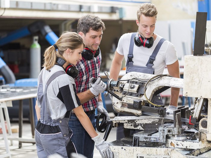 Giornata Internazionale dell’Educazione: la formazione professionale come fattore determinante Tre operai lavorano insieme a una sega a nastro metallica nell'officina