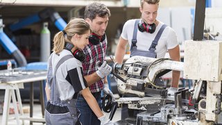 News Tre operai lavorano insieme a una sega a nastro metallica nell'officina