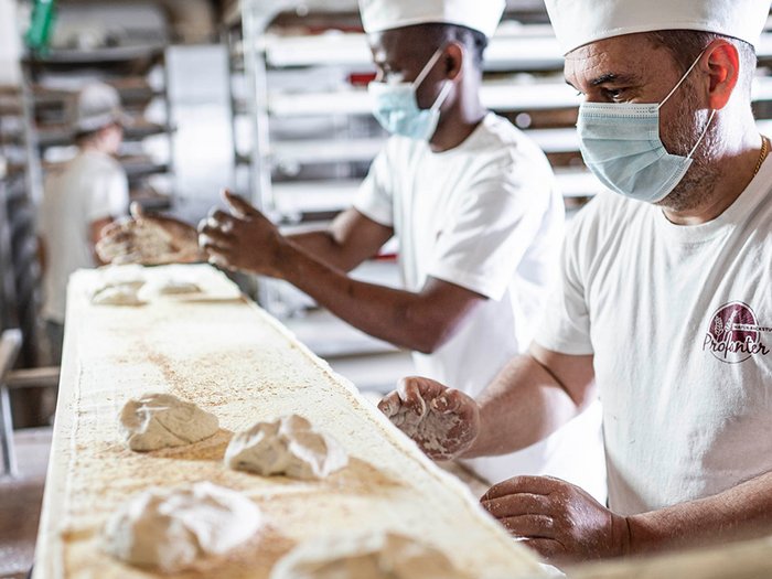 lvh-Chef: „Einen zweiten Lockdown können wir uns nicht leisten“ Bäcker mit Mundschutz formen Teigstücke in Handwerksbäckerei