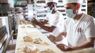 News Bäcker mit Mundschutz formen Teigstücke in Handwerksbäckerei
