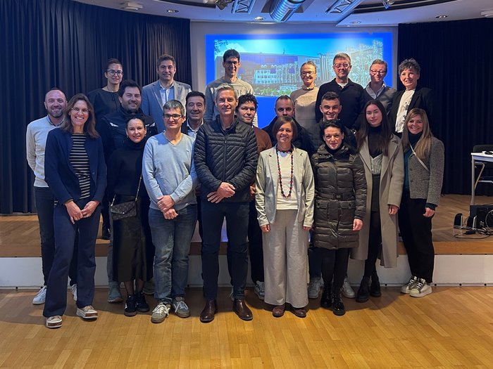 Treffpunkt Schule in Bruneck: Gemeinsam Perspektiven stärken und Ausbildung weiterentwickeln Gruppenfoto von 21 Erwachsenen in einem Veranstaltungsraum vor einer Projektionsleinwand