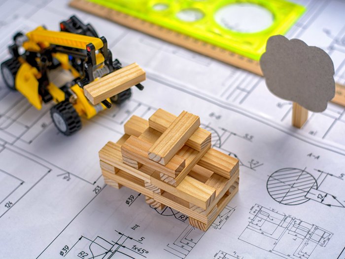 Gemeinsames Webinar von WOBI und lvh Spielzeug-Bagger hebt Holzblöcke auf Bauplan mit Lineal und Baumfigur