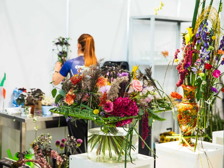 Fioristi Composizioni floreali colorate in vasi di vetro su piedistalli davanti a una donna con coda di cavallo