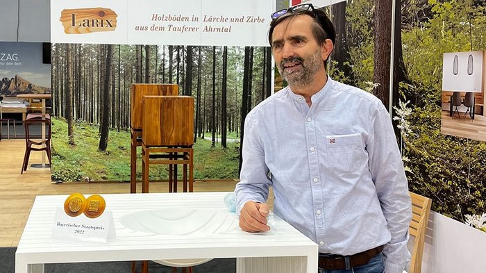 Reinhold Stoll; © lvh.apa Mann präsentiert weißen modernen Tisch mit Bayerischem Staatspreis auf Messe