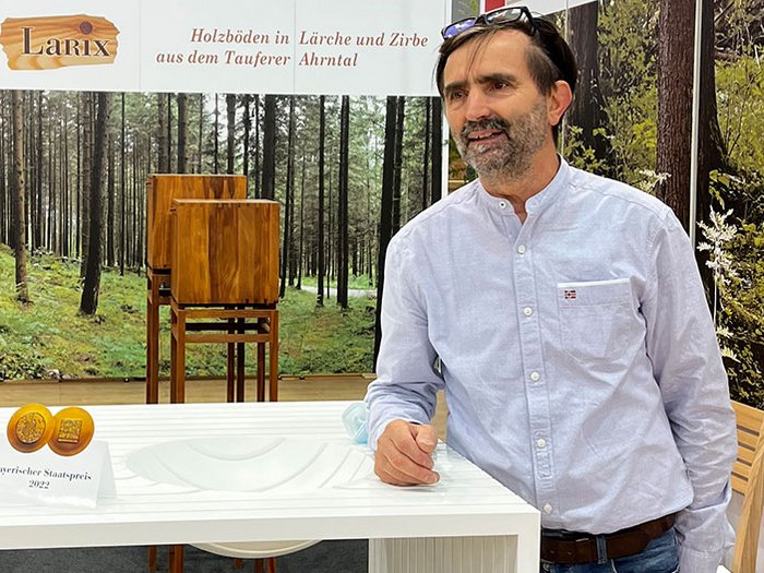 Reinhold Stoll; © lvh.apa Mann präsentiert weißen modernen Tisch mit Bayerischem Staatspreis auf Messe