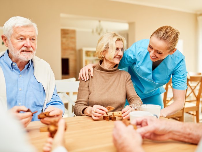 Vita assistita per anziani nel quartiere di Maia Alta a Merano Operatore sanitario sorride mentre anziani giocano a un gioco da tavolo assieme