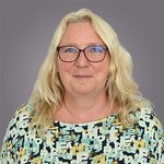 Das lvh-Team Porträt einer lächelnden Frau mit blonden Haaren und Brille vor grauem Hintergrund