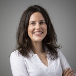 Das lvh-Team Lächelnde Frau mit braunen Haaren und weißer Bluse vor grauem Hintergrund