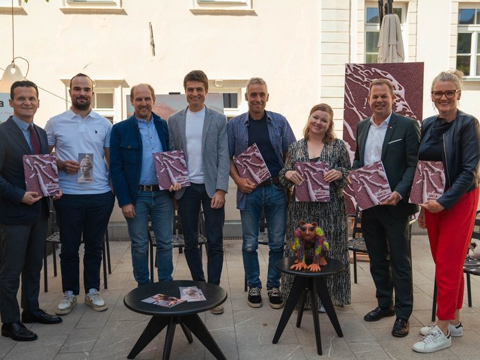 UNIKA präsentiert die 31. Kunstmesse Gruppe von acht Personen hält Broschüren bei einer Veranstaltung im Innenhof