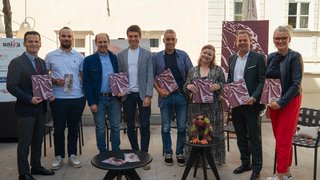 News Gruppe von acht Personen hält Broschüren bei einer Veranstaltung im Innenhof