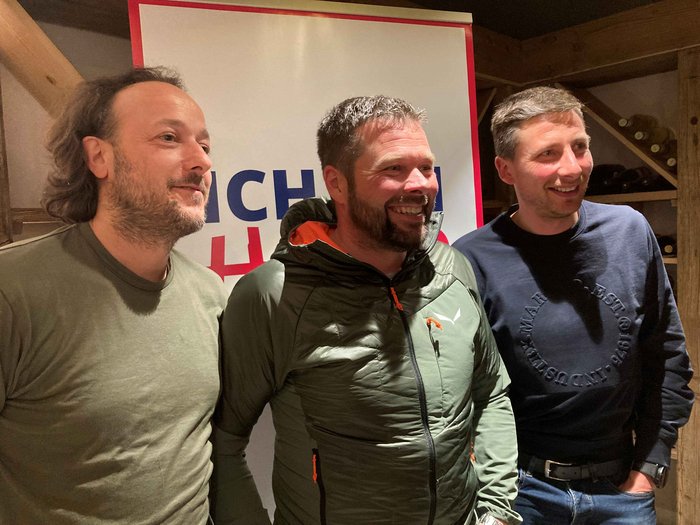 Beständigkeit in Welsberg-Taisten Drei Männer lachen vor einem Banner bei einer Veranstaltung