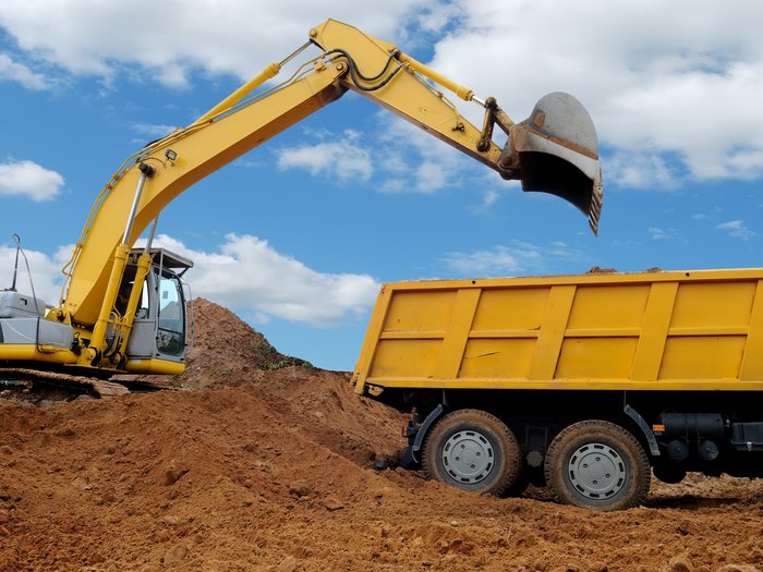 Barometro dell’economia IRE – Primavera 2025 Costruzioni: clima di fiducia positivo nonostante la debole domanda Escavatore giallo carica terra in un camion giallo sotto un cielo blu