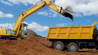 News Gelber Bagger lädt Erde in einen gelben Muldenkipper unter blauem Himmel