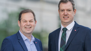 News Zwei Männer in Anzügen lächeln vor unscharfem Hintergrund