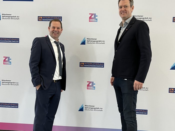 Una delegazione sudtirolese visita la fiera bavarese "Zukunft Handwerk" Due uomini in abito davanti al muro con scritto Münchener Spitzengespräch der Deutschen Wirtschaft