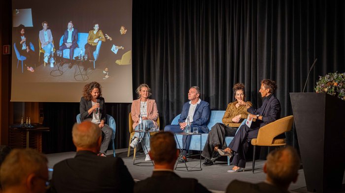 Crescita in equilibrio Cinque persone su palco in discussione con pubblico seduto di fronte