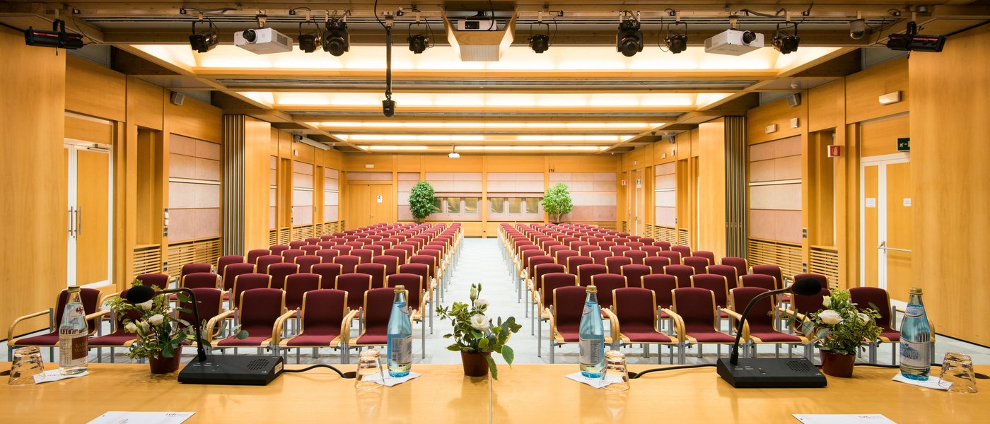 Vermietung Seminarräume Leerer Konferenzraum mit Stühlen und einem Tisch mit Mikrofonen und Wasserflaschen