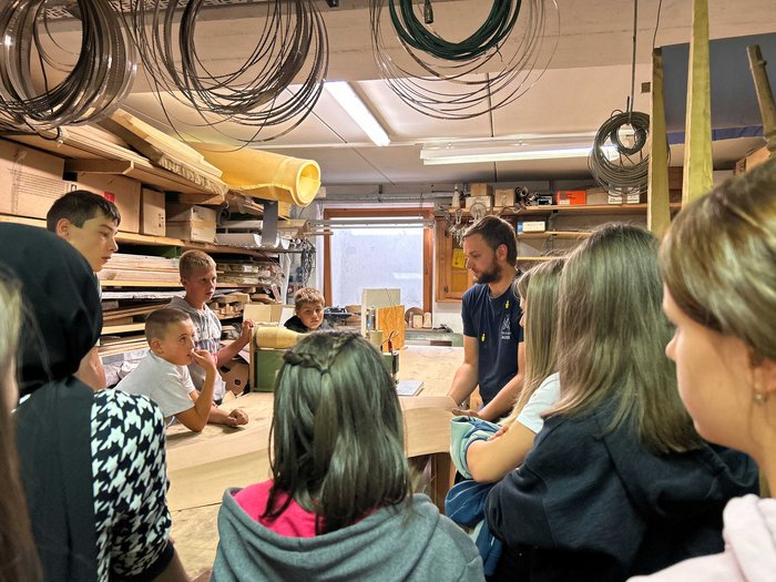 Praxis statt Theorie: Schulbesuche bei Handwerksbetrieben in St. Leonhard Gruppe Kinder lernt in Werkstatt von einem Mann Holzbearbeitung