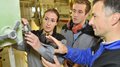 3670 neue junge Fachkräfte Ausbilder zeigt zwei Auszubildenden die Bedienung einer Maschine in Werkstatt