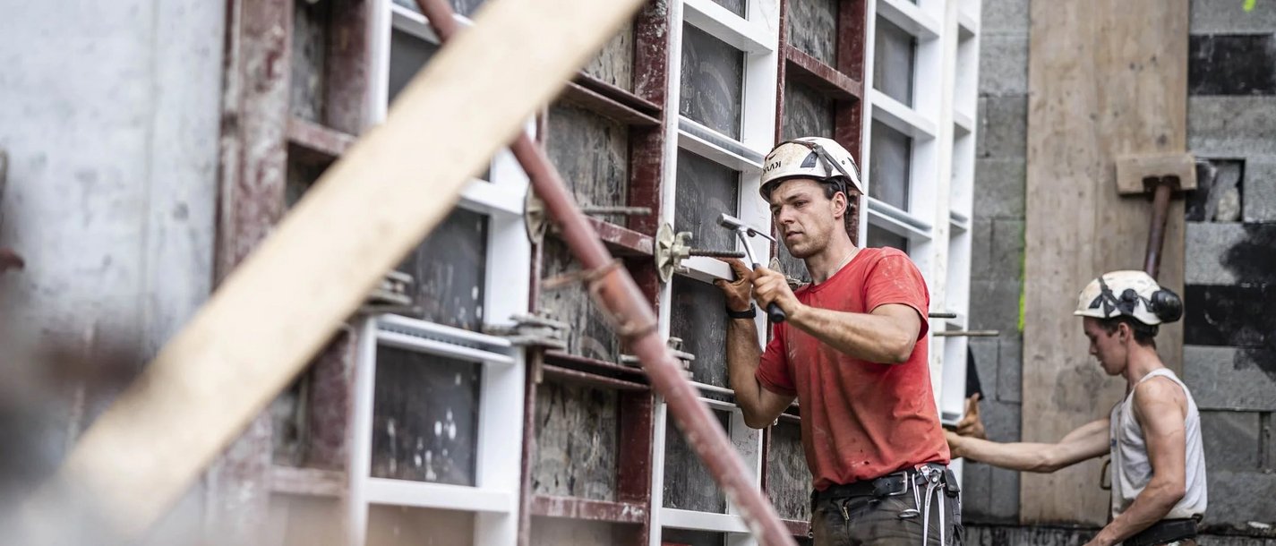 Arbeitssicherheit Zwei Bauarbeiter mit Helmen arbeiten an einer Betonwand auf einer Baustelle