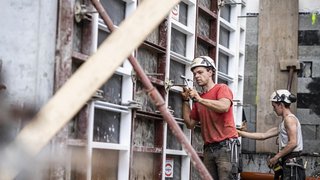 News Zwei Bauarbeiter mit Helmen arbeiten an einer Betonwand auf einer Baustelle