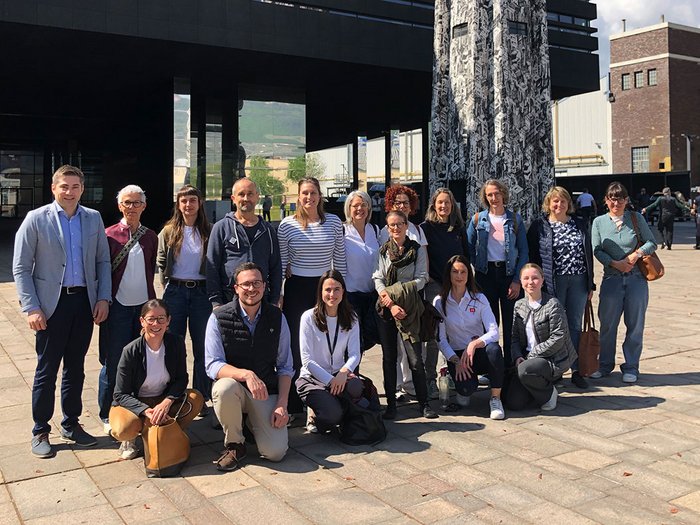 Avviare un’impresa: perché anche la migliore idea fallisce senza una strategia Foto di gruppo di 19 persone davanti a edificio moderno con opera d'arte