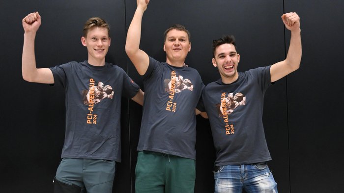 Südtirol begeistert beim Wettkampf der Fliesenleger/innen in Bozen! Drei Männer feiern mit PCI-Alpen Cup 2024 T-Shirts vor schwarzem Hintergrund