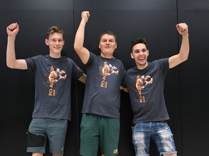 Südtirol begeistert beim Wettkampf der Fliesenleger/innen in Bozen! Drei Männer feiern mit PCI-Alpen Cup 2024 T-Shirts vor schwarzem Hintergrund