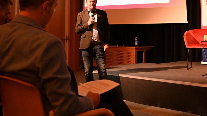 "La città che desideri": un incontro per il futuro di Bolzano Uomo parla con microfono davanti al pubblico in sala conferenze con presentazione