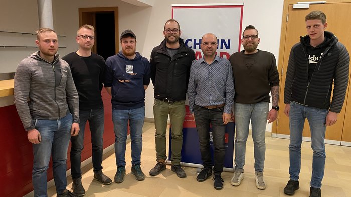 Lajen: Wir sind Handwerk! Sieben Männer stehen in einem Raum vor einem Maschinenhandwerksbanner