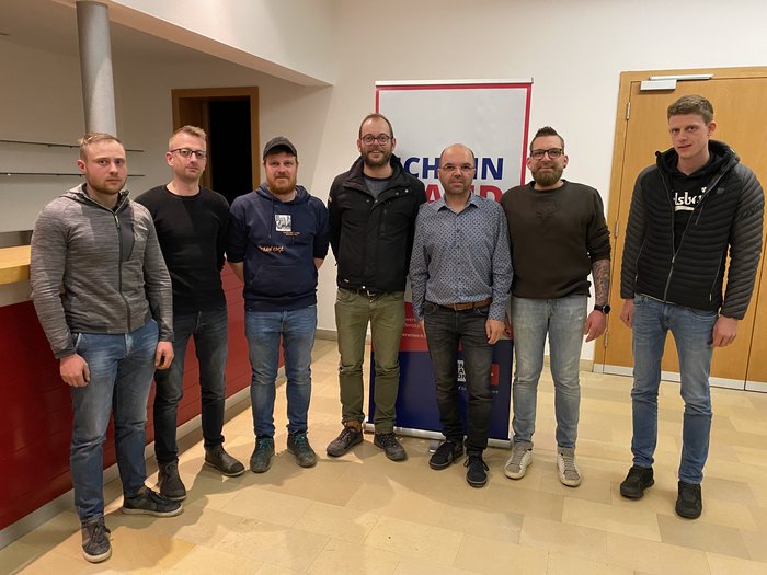 Lajen: Wir sind Handwerk! Sieben Männer stehen in einem Raum vor einem Maschinenhandwerksbanner