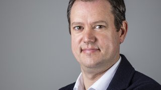 News Porträt eines lächelnden Mannes vor grauem Hintergrund