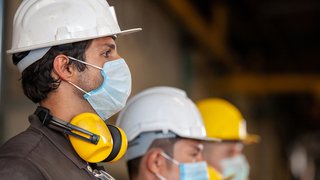 News Bauarbeiter mit Schutzhelmen, Mundschutz und Gehörschutz in einer Produktionsumgebung