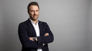 News Ritratto di uomo sorridente con le braccia incrociate su sfondo grigio