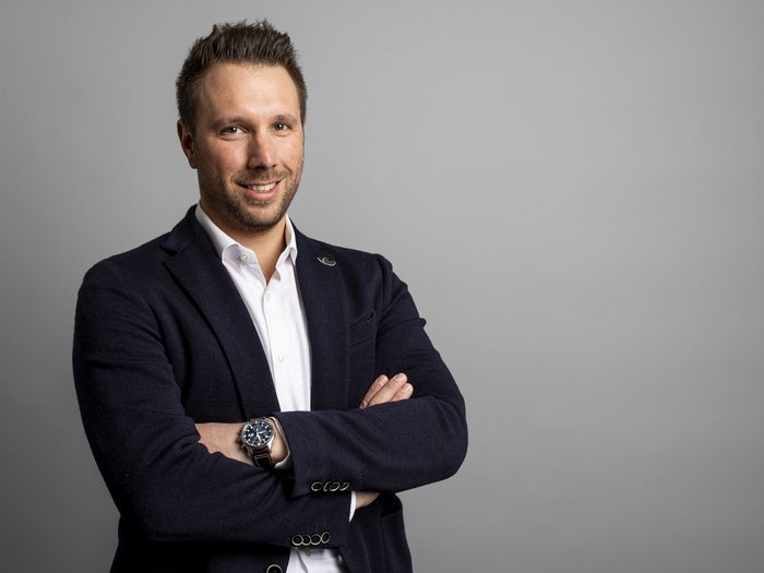 Neuer Kollektivvertrag für das Bauhandwerk unterzeichnet Porträt eines lächelnden Mannes mit verschränkten Armen vor grauem Hintergrund