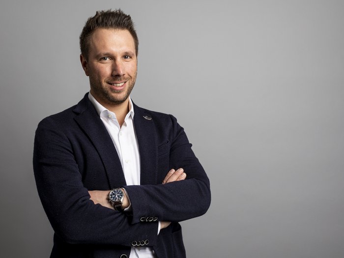 Neuer Kollektivvertrag für das Bauhandwerk unterzeichnet Porträt eines lächelnden Mannes mit verschränkten Armen vor grauem Hintergrund